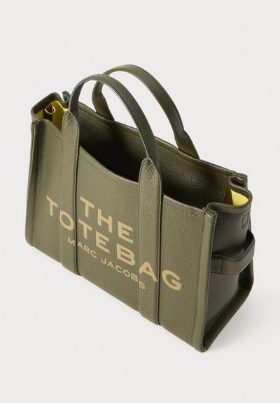 Olijfgroene leren tote bag met gouden letters, twee stevige handvatten, gestructureerd ontwerp en gele interieurdetails. Accenten aan de zijkanten.
