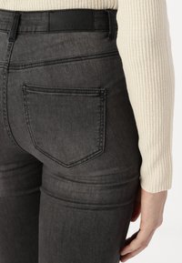 Mørkegrå denimjeans med en baklomme og et sort lærbelte. Tøyet har en glatt tekstur med minimal falming.