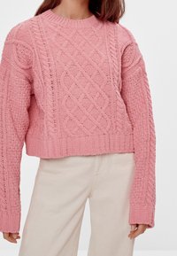 Suéter de punto trenzado rosa con cuello redondo y diseño corto. Presenta patrones texturizados y puños y dobladillo en canalé. Tela suave y lisa.