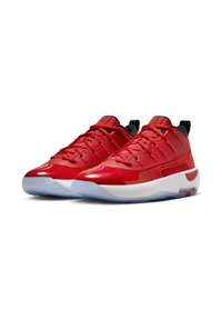 Czerwone buty sportowe z błyszczącym wykończeniem, z siateczkowymi wstawkami, wyściełanym kołnierzem i przezroczystą gumową podeszwą. Akcenty w kolorze czarnym i białym.