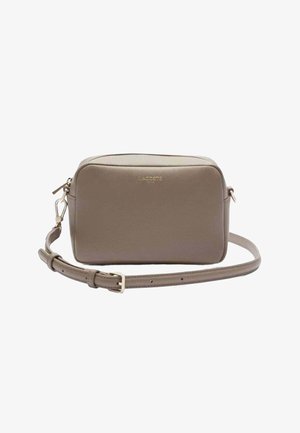 Sac bandoulière rectangulaire taupe avec sangle réglable et logo Lacoste doré sur le devant, sur fond blanc.