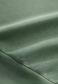 Tissu vert texturé avec une finition lisse, présentant des plis subtils et un doux éclat, affichant une couleur uniforme sans motifs.