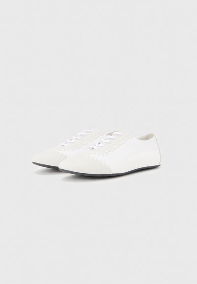 Λευκά φλατ παπούτσια από απαλό υλικό, με μυτερή μύτη και λευκά κορδόνια. Διακοσμητικές ραφές κατά μήκος των πλευρών προσθέτουν λεπτομέρεια.