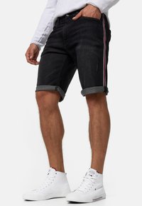 Shorts en denim noir avec poignets retroussés, présentant des bandes latérales colorées en rouge, blanc et bleu. Design classique à cinq poches.