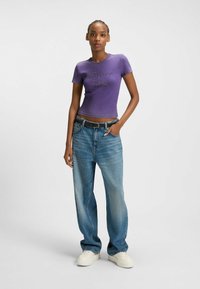 Paars fitted T-shirt met de tekst "Forever...", gecombineerd met hoge, losse blauwe denim jeans en witte platform sneakers.
