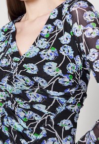 Schwarz-blumiges Kleid mit V-Ausschnitt, verziert mit blauen und grünen Blumen auf durchscheinendem Stoff, der einen strukturierten Lagen-Effekt erzeugt.