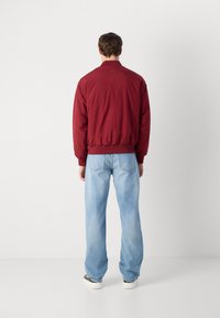Red bomber jacket with ribbed hem and cuffs, paired with light blue straight-leg jeans. Back view shows minimal design and soft texture.
