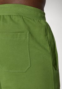 Calções de algodão verdes com uma cintura elástica, apresentando um bolso traseiro de forma retangular e detalhes de costura bem acabados.