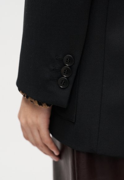 Μαύρο εφαρμοστό σακάκι με τρία μαύρα κουμπιά στο μανίκι, με φόδρα σε animal print λεοπάρ στην άκρη του μανικιού.