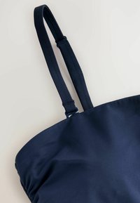 Marineblaue Umhängetasche aus glattem Stoff mit zwei verstellbaren Riemen und schlichtem Design. Inklusive eines Metallverschlusses.