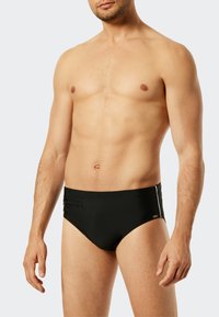 Schwarze Schwimmbrieft mit glatter Textur, ausgestattet mit einer seitlichen Reißverschlusstasche und kontrastierenden weißen Akzenten an den Seiten. Klassisches Schnittdesign.