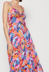 Robe maxi florale avec un détail en nœud et une découpe à la taille. Couleurs vives comprenant du rose, du bleu et de l'orange avec des motifs feuillagés.