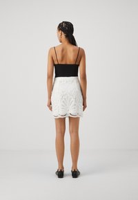 Haut sans manches noir associé à une jupe en dentelle blanche avec un ourlet festonné et un motif floral, complété par des chaussures noires à cheville.