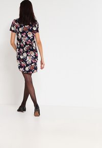 Šaty s květinovým vzorem v tmavě námořnické barvě, s krátkým rukávem, do délky kolen, s volným střihem. Modelka má na sobě černé neprůhledné punčocháče a boty.