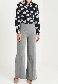 Woman wearing gray wide-leg trousers and a navy button-up shirt with a pale pink floral pattern, paired with beige heels.