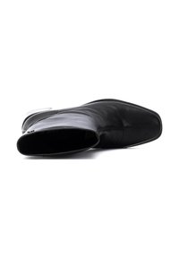 Botte de cheville en cuir noir avec un bout pointu, texture lisse, zip sur le côté et semelle plate. Design minimaliste sans motifs visibles.