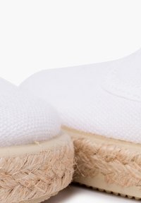 Espadrilles en toile blanche avec une finition texturée, présentant une semelle en jute et un design à bout arrondi. Légères et décontractées en apparence.
