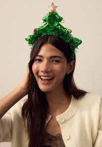 Green Christmas tree headband with sequin accents, pom-poms, and a gold star. Worn with a cream cardigan. Smooth texture, vibrant color.