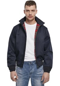 Veste bombardier navy avec une doublure en carreaux rouges, des poignets côtelés et un col montant. Fabriquée en tissu lisse avec une fermeture éclair.