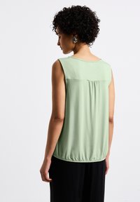 Top senza maniche verde chiaro realizzato in morbido tessuto, con scollatura rotonda, arricciatura sul retro e orlo leggermente elastico.