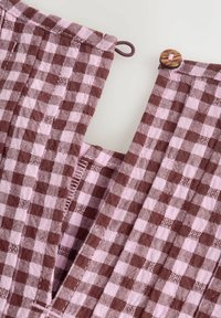 Material în carouri maro și roz cu design cu decolteu în V, având un nasture și un detaliu elastic la nivelul gâtului. Țesătura texturată este vizibilă.