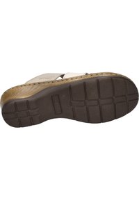 Brown rubber outsole with a textured tread pattern; features a raised logo and serrated edge. Light-colored strap design above.