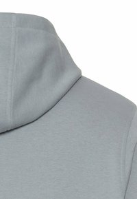 Nahaufnahme des Rückens eines hellgrauen Hoodies, der die Kapuze und einen Teil des Schulterbereichs zeigt und die Textur des Stoffes hervorhebt.