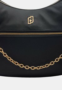 Borsa a tracolla in tessuto nero con cima curva, caratterizzata da un accento in catena dorata e da una zip dorata lungo la parte anteriore, che mostra un logo.