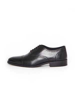 Chaussure de ville Oxford pour hommes en cuir noir avec détails brogue, laçage fermé et talon bas sur fond blanc.