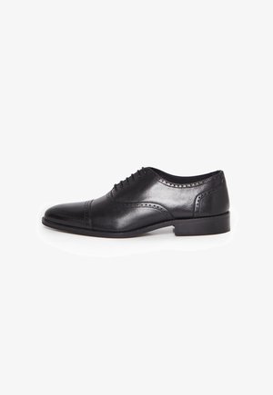 Chaussure de ville Oxford pour hommes en cuir noir avec détails brogue, laçage fermé et talon bas sur fond blanc.