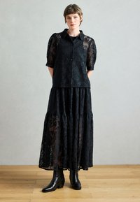 Μαύρη δαντελένια μπλούζα με κοντά μανίκια, σε συνδυασμό με φούστα πολλαπλών στρωμάτων που ταιριάζει. Και τα δύο διαθέτουν περίπλοκα σχέδια· φοριούνται με μαύρα μποτάκια αστραγάλου.