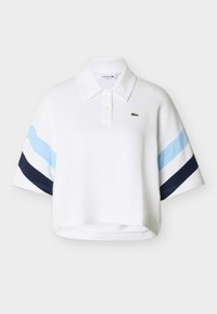 Polo blanc court avec des rayures diagonales bleu et marine sur les manches, patte à deux boutons et petit logo crocodile vert sur la poitrine.