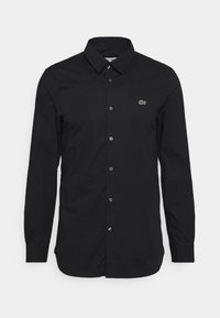 Camicia nera con bottoni realizzata in tessuto morbido, con colletto classico, maniche lunghe e un piccolo logo verde sul petto.
