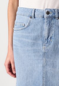 Lys blå denimskjørt med rett snitt, som har knappelukking, beltehemper og subtil fading. Lommene på siden er synlige.