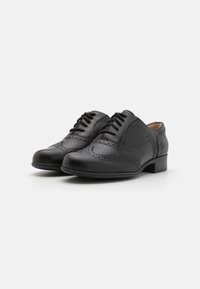 Scarpe in pelle nera con design allacciato, dettagli brogue, punta arrotondata e tacco basso a blocco. Texture liscia con accenti perforati.