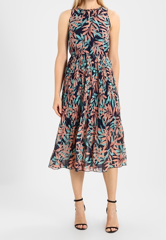 Abito lungo floreale con sfondo blu navy e motivi di foglie rosa e teal, design senza maniche e vita arricciata, abbinato a sandali neri.