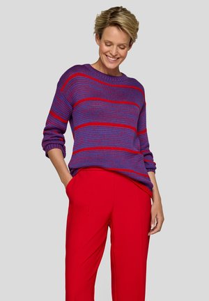 Lila Strickpullover mit roten horizontalen Streifen, rundem Ausschnitt und umgeschlagenen Ärmeln, kombiniert mit roten, weit geschnittenen Hosen.