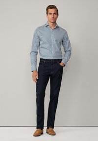 Blue and white striped button-up shirt, dark jeans, and tan loafers. Fit is tailored, with long sleeves and single chest pocket.