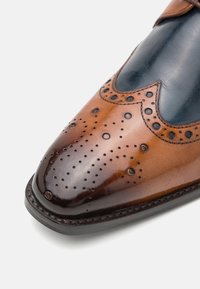 Scarpa in pelle marrone con accenti blu scuro, design wingtip, perforazioni decorative sulla punta e una finitura liscia e lucida.