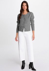 Grauer gestrickter Cardigan mit Rundhalsausschnitt, Knopfleiste und langen Ärmeln, kombiniert mit weißen weiten Hosen und schwarzen Stiefeletten.