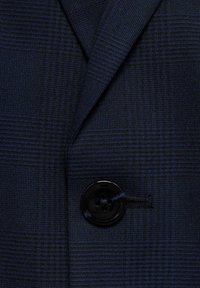 Mörkblå rutigt blazer tyg med en texturerad väv, med glansiga svarta knappar som detalj. Nära bild av slagområdet.