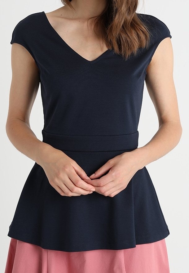 Mujer vestida con una blusa ajustada de manga corta en color azul marino con escote en V y cinturilla peplum, combinada con una falda rosa.