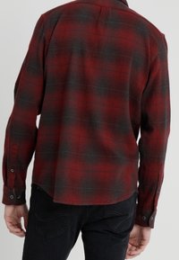 Camicia a quadri rossa e nera in flanella con maniche lunghe, polsini con bottoni e orlo leggermente curvo. Tessuto morbido con motivo intrecciato.