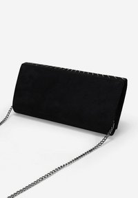 Clutch de ante negro con una correa de cadena plateada. Presenta una forma rectangular elegante y un sutil detalle de costura a lo largo del borde superior.