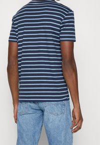 Navy blue and light blue striped short-sleeve T-shirt, made of cotton, featuring a crew neck and a relaxed fit, paired with light denim jeans.