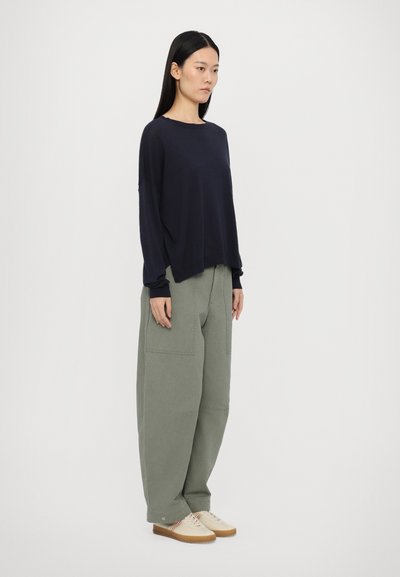 Tumši zilas krāsas garās piedurknes krekls ar brīvu piegriezumu, saskaņots ar brīviem olīvu zaļas krāsas kravas biksēm un gaišām kedām. Vienkāršs, bez pievienojumiem dizains.