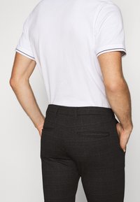 Biała koszulka z krótkim rękawem z kontrastowym wykończeniem rękawów, połączona z ciemnoszarymi, teksturowanymi spodniami z tylnymi kieszeniami i dopasowanym krojem.