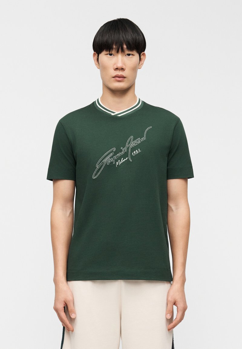 Πράσινο βαμβακερό t-shirt με V-λαιμό και αντίθετη λευκή διακόσμηση. Διαθέτει κεντημένο λογότυπο μπροστά, κοντά μανίκια και κανονική εφαρμογή.