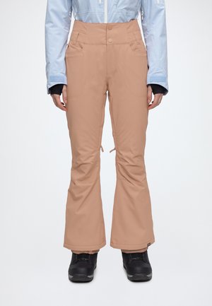 Un modèle porte un pantalon de neige beige évasé, à taille haute boutonnée, une veste bleu clair et des bottes de neige noires sur fond blanc.