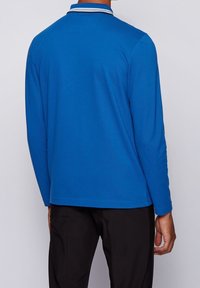 Långärmad polo skjorta i livfull blå bomull, med en kontrasterande krage med vit och svart kant, slät textur och figurnära design.